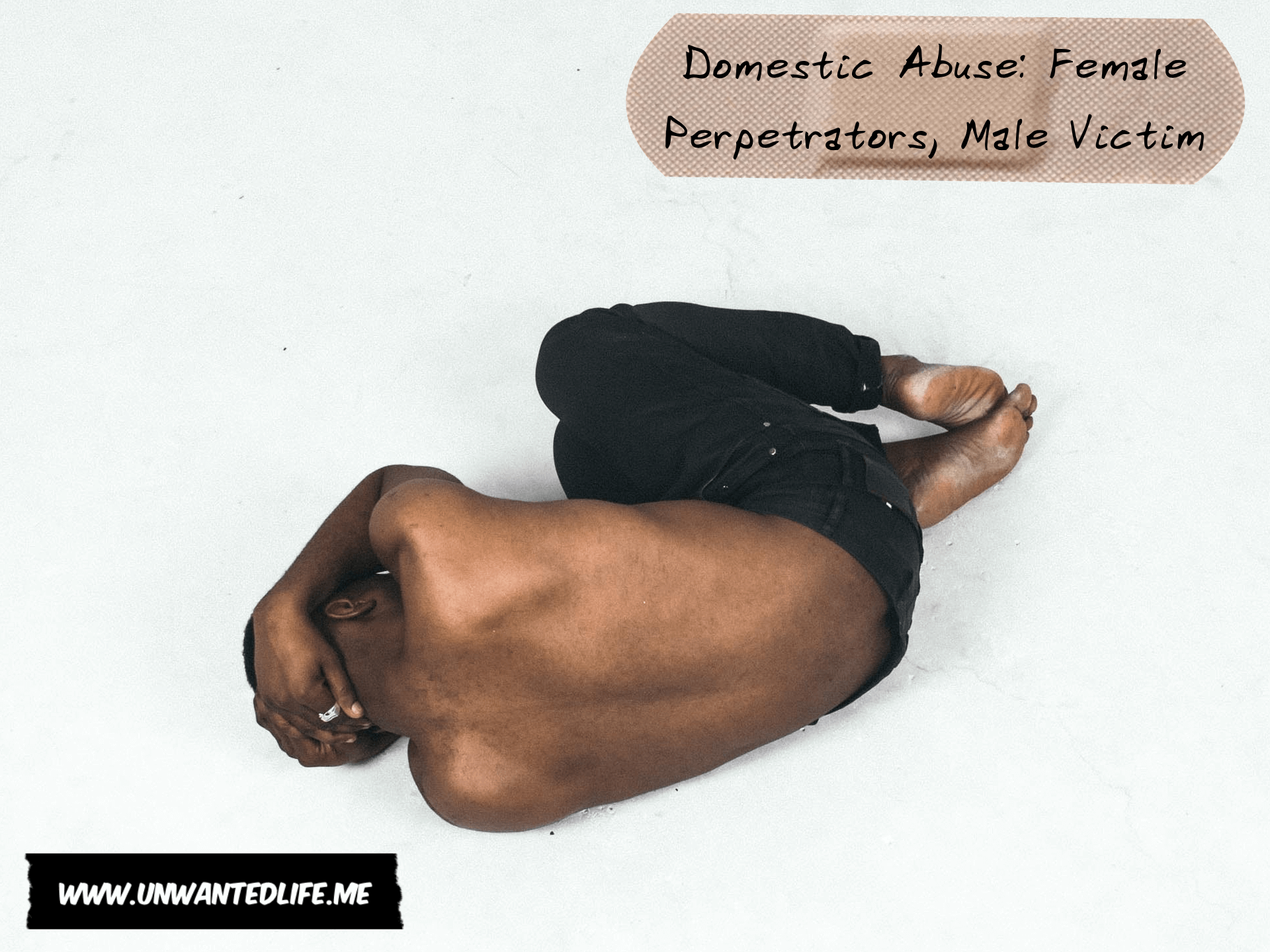 Photo of a topless black man laying on the floor covering himself as if to protect himself on a cold white floor with the title of the article - Domestic Abuse Female Perpetrators, Male Victim - in the top right corner of the image
