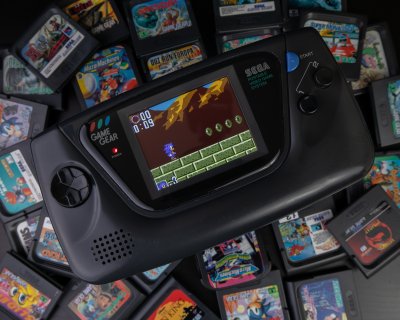 A photo of SEGA's hand held game console, the Game Gear, resting on a pile of Game Gear game cartridges - Retro Gaming