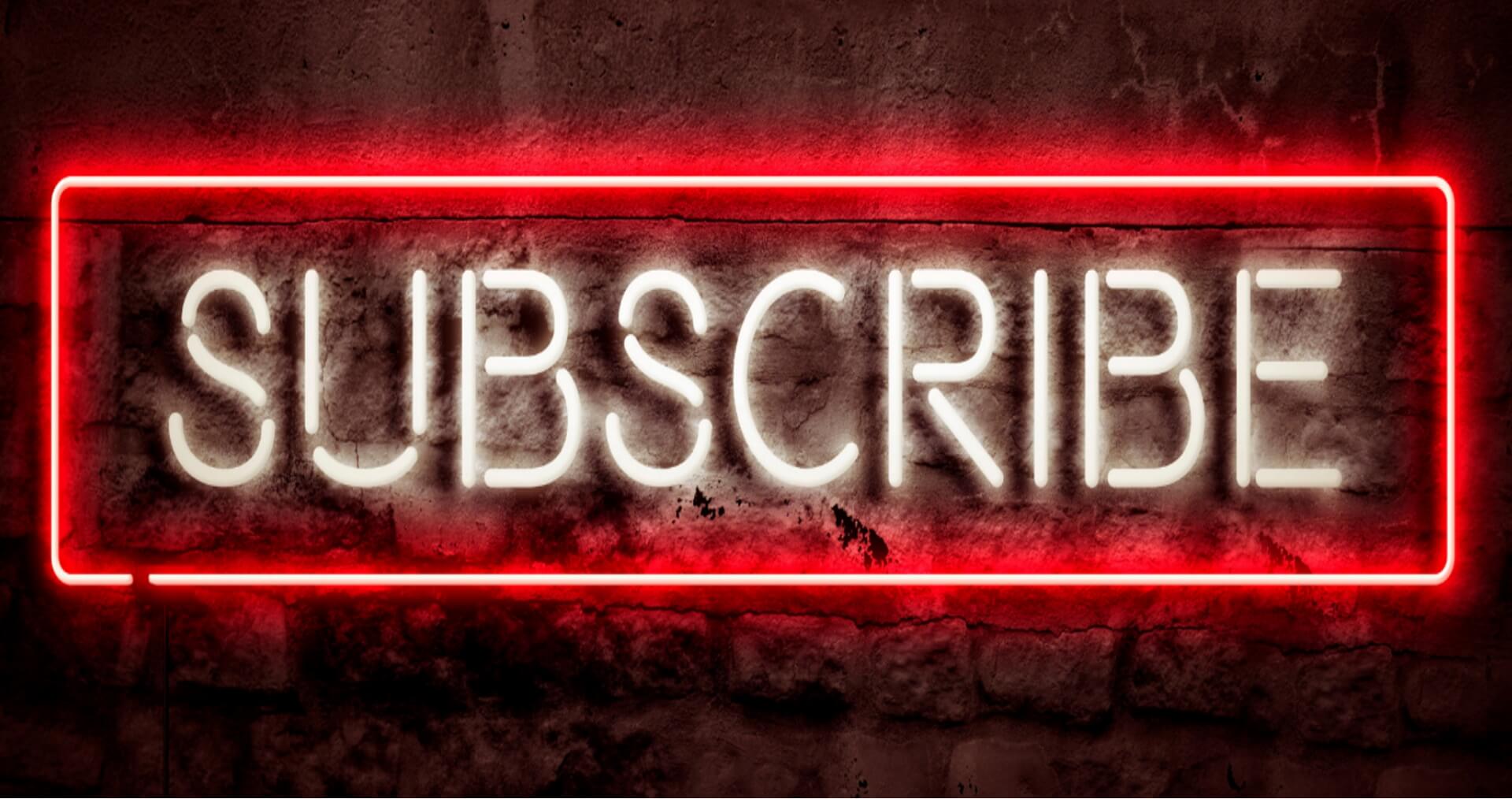 Neon sign that says - Subscribe - in white neon tubing with a red neon tubing boarder on a dark black brick wall
