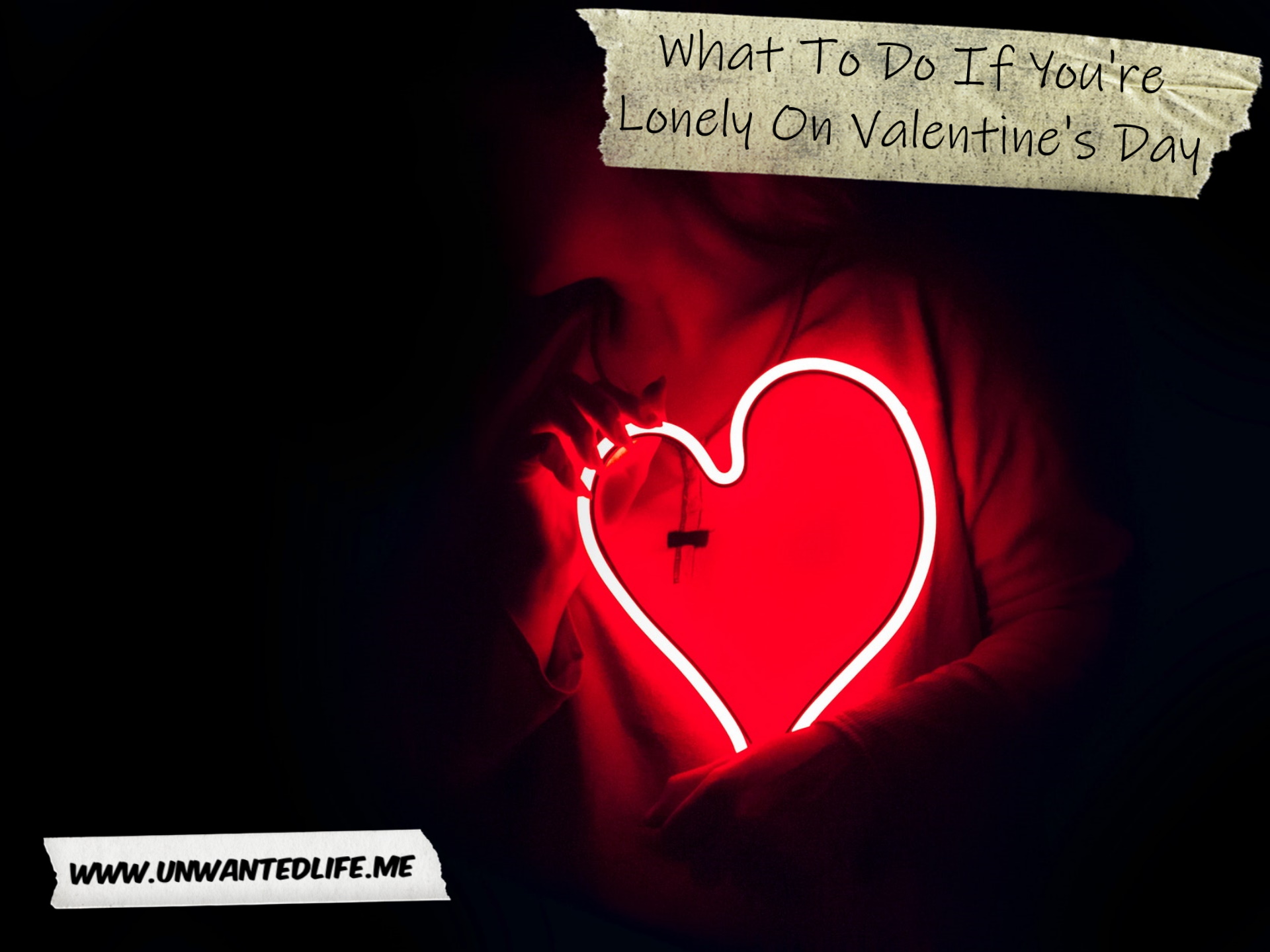 A photo of a woman in a black room being partially illuminated by a red light in the shape of a heart to represent the topic of the article - What To Do If You're Lonely On Valentine's Day