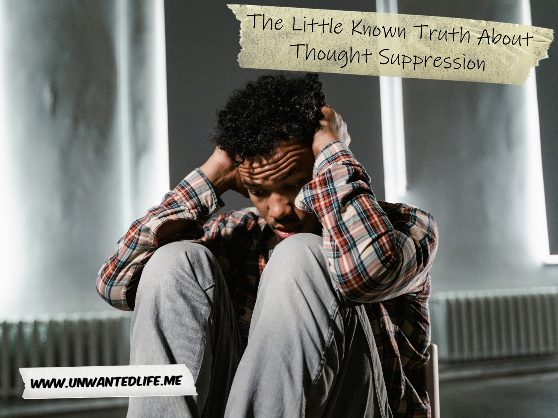 A photo of a Black man sitting on a chair in an empty room, with his knees to his chest and his hands over his ears, all while looking distressed. This is to represent the topic of the article - The Little Known Truth About Thought Suppression