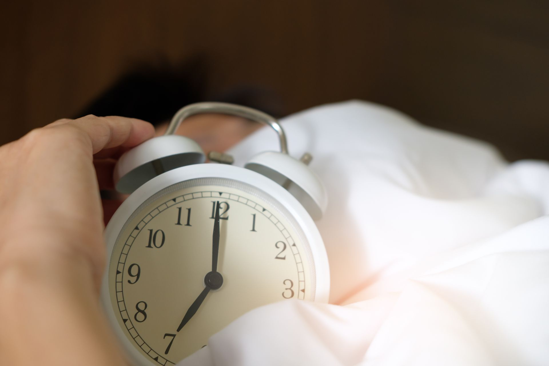 Someone in bed with an alarm clock in front of their face to represent the topic of this article - How Establishing A Morning Routine Overrode My Depression