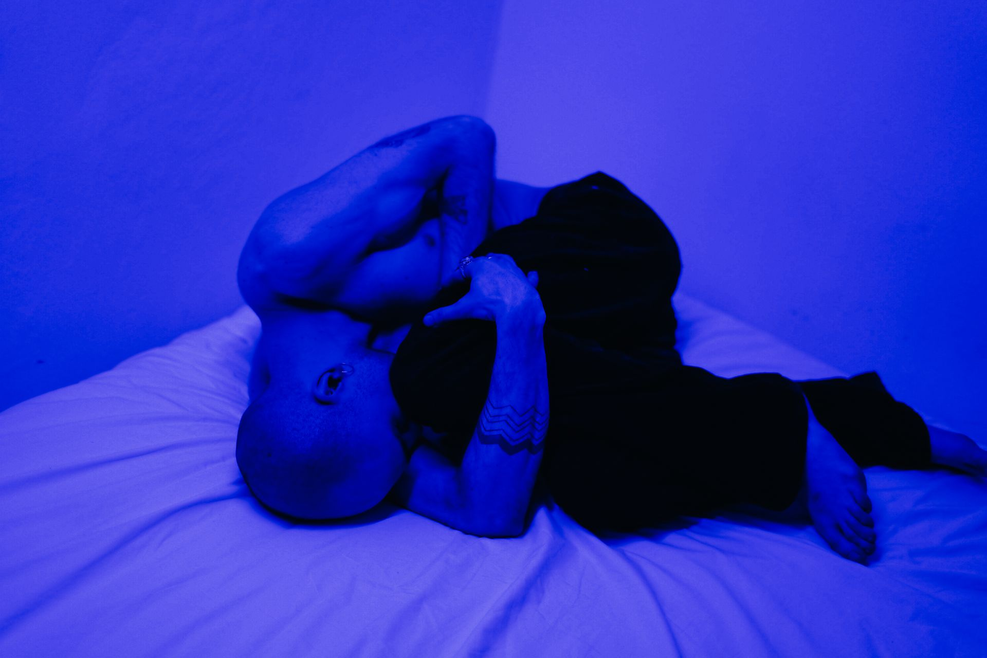 A blue washed photo of a man curled up in bed to represent the topic of the article - My Somewhat Unfortunate Experiences With Withdrawals